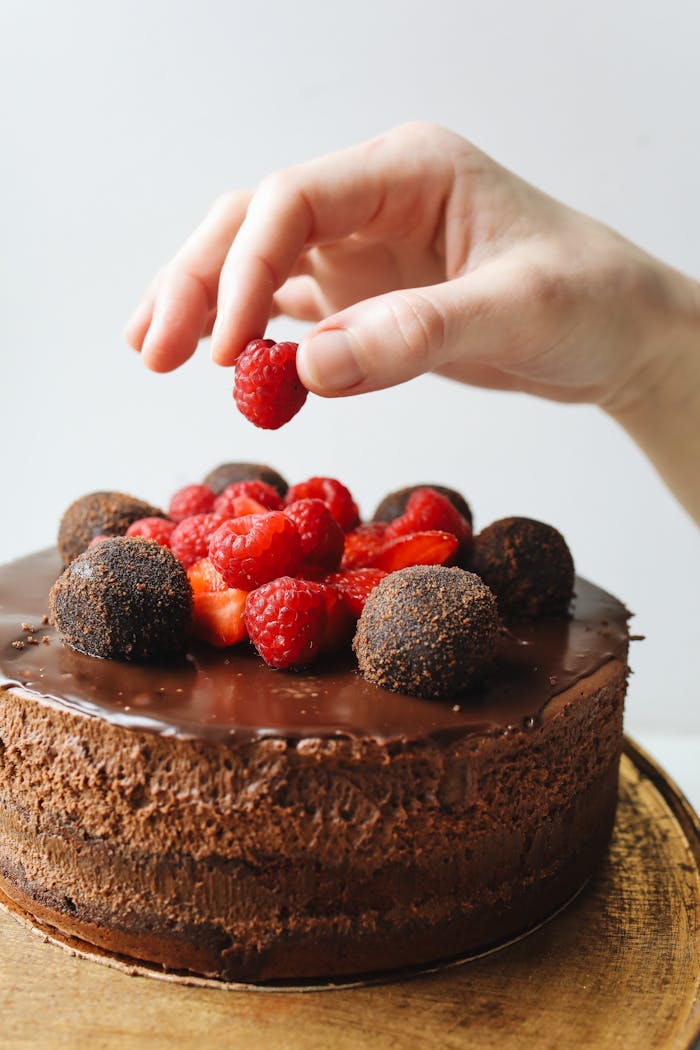 Crafting Captivating Headlines: Your awesome post title goes here Close-up of a hand decorating a chocolate cake with raspberries and truffles.