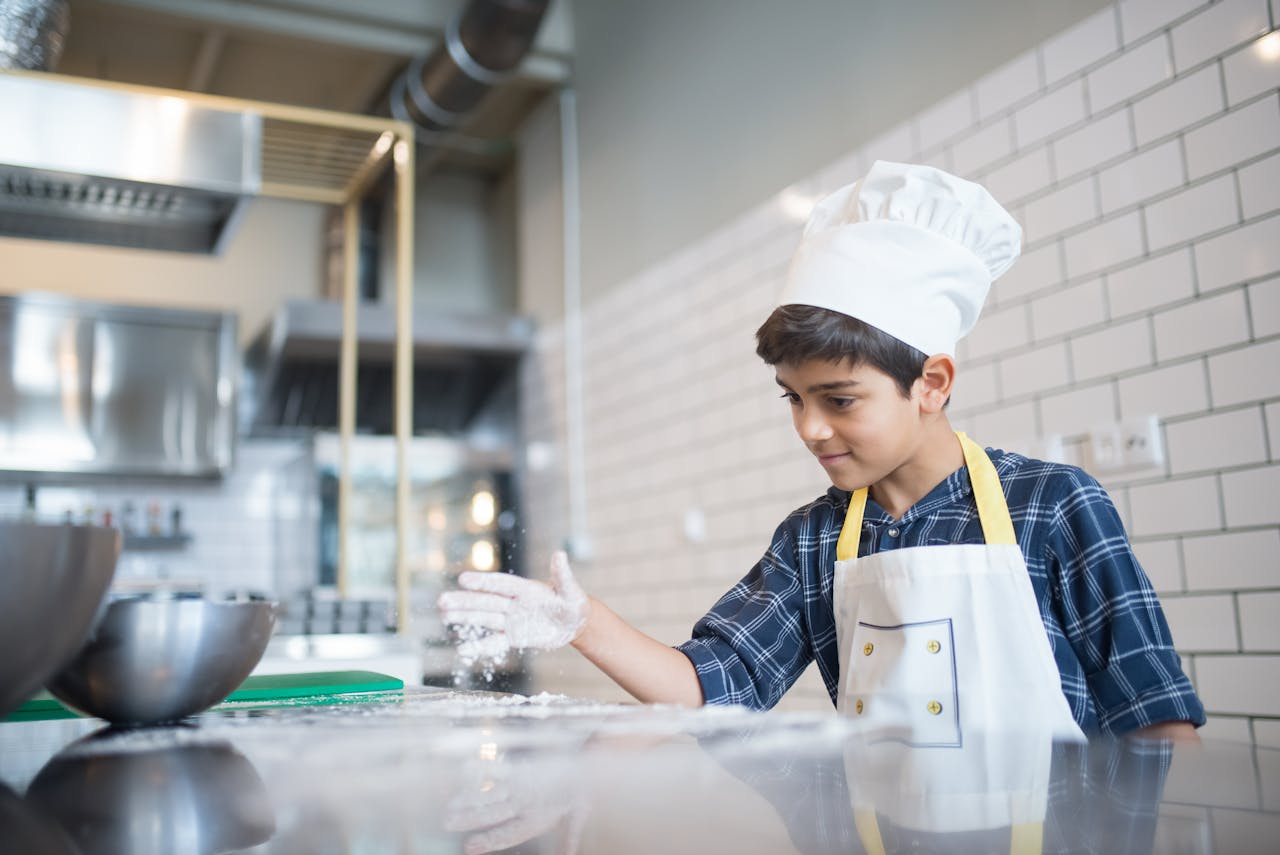 Mastering the First Impression: Your intriguing post title goes here A young boy in a chef's hat and apron sprinkles flour on a kitchen countertop, showcasing his cooking skills.